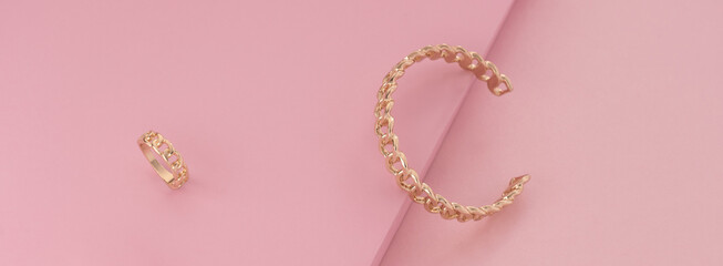Panorama of Chain shape golden ring and bracelet on pink background