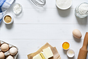 Baking ingredients: flour, eggs, sugar with a rolling pin on a light white wood background. With...