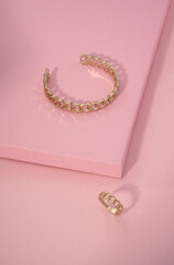 Chain shape golden bracelet and ring on pink color background