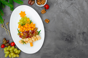 Cheese Christmas tree with fresh grapes and rosemary on a white plate on a concrete background. Food idea for Christmas and New Year. Top view.