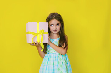 The child has a happy face holding a gift box on a yellow background. The kid is happy, loves birthday and holidays.