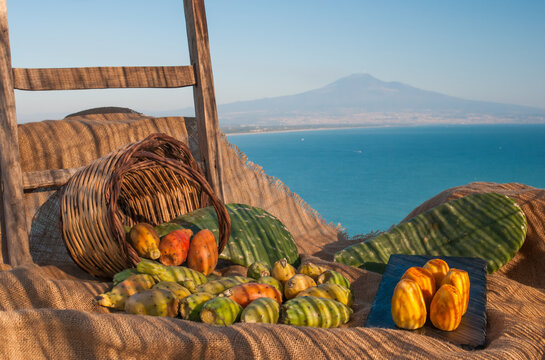 Prickly pears and a wicker baslet on a piece of jute, blue sea and Mount Etna in the background
