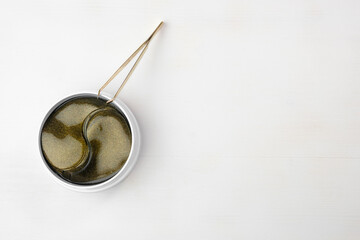 Top view on the jar with gold collagen hydrogel eye patches and tweezers on the white background with copy space.