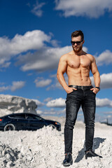 Strong athletic man fitness model. Guy with nacked torso showing six pack abs. Luxury black car on the background. Half length photo.