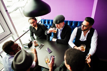 Group of handsome retro well-dressed man gangsters spend time at club, sitting and drinking whiskey. Multiethnic male bachelor mafia party in restaurant.