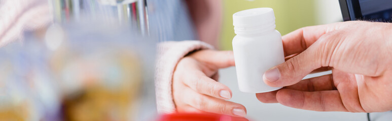 partial view of pharmacist giving bottle with medication to customer, banner