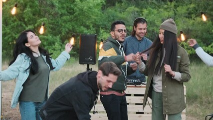 Medium shot of cheerful multi-ethnic friends dancing to music while dj playing in background at open-air cozy party on summer evening