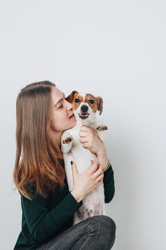 Cute young woman kisses and hugs her puppy jack russell terrier dog. Love between owner and dog. Isolated on white background. Studio portrait.