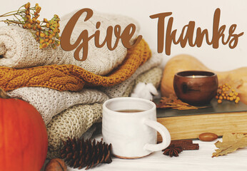 Give Thanks text handwritten on warm tea, pumpkins and spices at cozy sweaters, autumn leaves, candle. Happy Thanksgiving greeting card. Seasons greetings.
