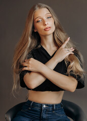 Close up studio portrait of pretty blonde woman in black top sitting on chair. Blue eyes, young and...