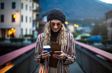 Blonde girl with cellphone and coffee on the bridge.