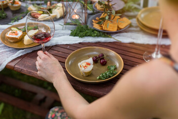 Female hand holding a glass of red wine at a rustic outdoor party. Plated savory muffin and cherries.