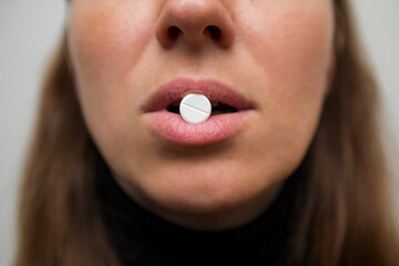 Womans lips hold a large white round pill. Healthcare concept with medicines. Woman taking a tablet...
