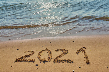 Year 2021 inscription on a tropical sandy beach with waves and foam on a background.