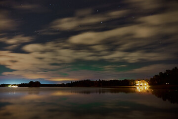 Aurora borealis Northern lights behind the clouds on Littoinen lake, Finland with reflections on water.
