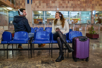 Cheerful couple sitting on train station and looking each other while listening music
