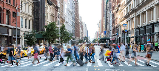 Busy street scene in New York City with groups of people walking across a crowded intersection on Fifth Avenue in Midtown Manhattan