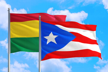 Puerto Rico and Bolivia national flag waving in the windy deep blue sky. Diplomacy and international relations concept.
