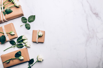 Fototapeta na wymiar Gift wrapped in recycled brown paper decorated with real fresh roses, on light background with minimalist style wrapping, top view flat lay, eco friendly and zero waste packaging