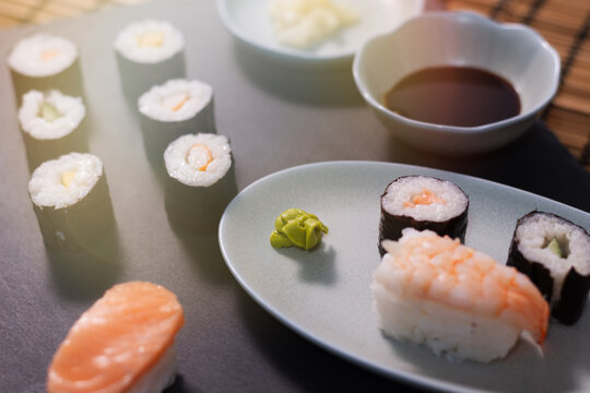 sushi on a tray and the slate, next to a bowl full of soy sauce, rice, salmon.