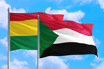 Sudan and Bolivia national flag waving in the windy deep blue sky. Diplomacy and international relations concept.