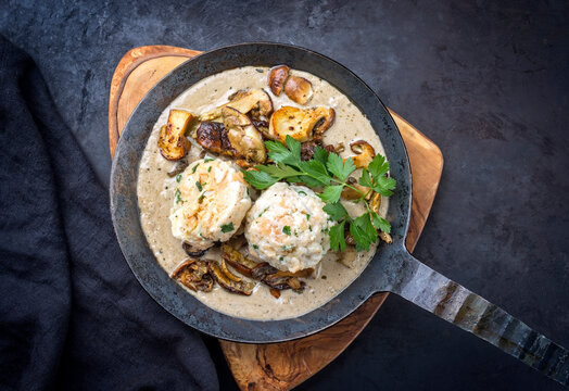 Modern Style traditionelle deutsche Steinpilze in Rahmsauce mit Semmelkn&ouml;del und Bratkartoffel serviert als Draufsicht in einer schmiedeeisernen Bratpfanne