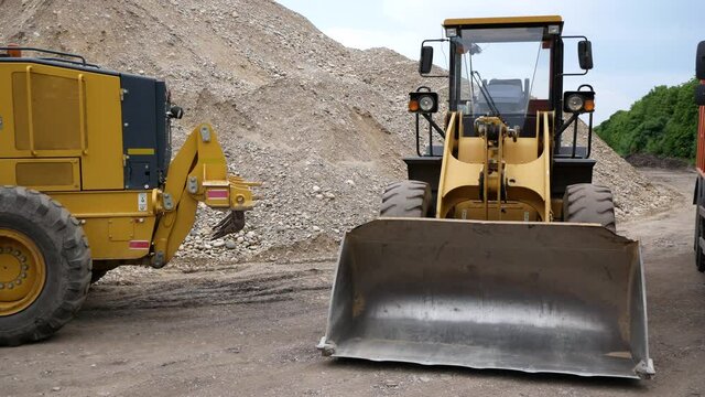 Large construction equipment is on construction site. Loader, grader, dump truck. Against background of huge mountains of rubble
