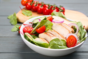 Delicious salad with chicken and vegetables on grey wooden table, closeup