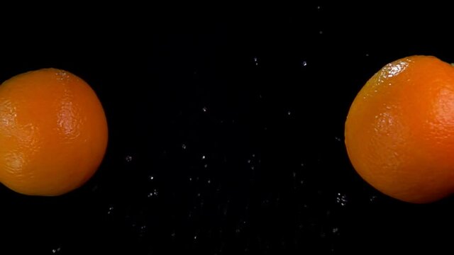 Two fresh oranges are flying and colliding with each other rising drops of water on the black background in slow motion