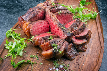 Modern Style traditionelles gegrilltes dry aged Wagyu Porterhouse Steak vom Rind serviert mit Salat und Gewürzen als Draufsicht auf einem Design Holz Board