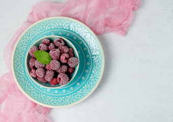 frozen raspberries.

Frozen raspberries in a blue plate on the left on a light concrete background with space for text on the right, top view close-up.