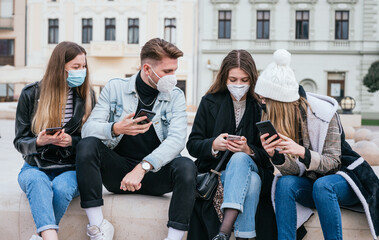 Group of young friends wearing masks and using their smart phones