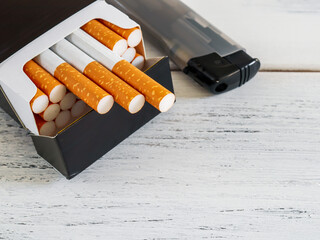 cigarette and lighter.
Black pack of cigarettes and gray lighter on the left on a wooden table with space for text on the right, top view close-up.
