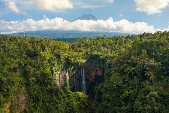 Aerial view of  Tumpak Sewu Waterfall in Java, Indonesia with Semeru Volcano in background.
