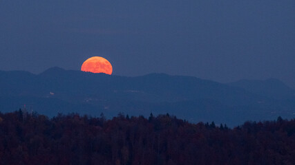 huge orange full moon rising behind a mountain ridge with layers of hills in the foreground...