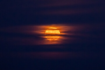 huge orange full moon peeking through misty clouds illuminating the sky around it, creating a...