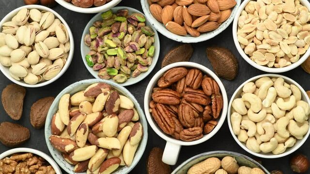  Assortment of various nuts in bowls and cups, top view on black, stone background, rotating