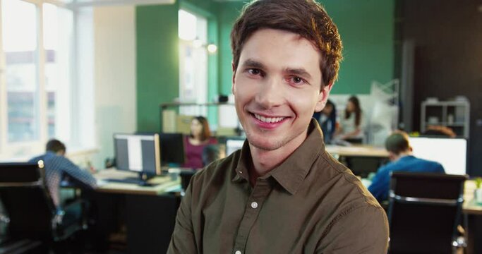 Close up portrait of young handsome office worker in brown shirt. Stylish man smiling at camera while standing in office.