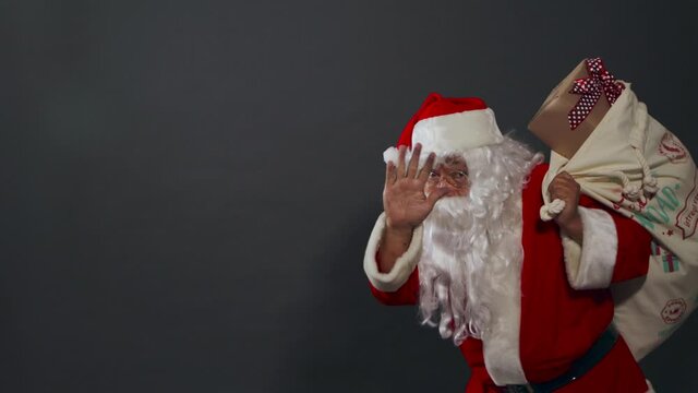 Papa noel con bolsa de regalos buscando saludando caminando alegre presentes
