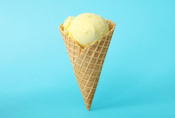 Delicious yellow ice cream in waffle cone on light blue background