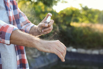 Man applying insect repellent onto hand outdoors, closeup