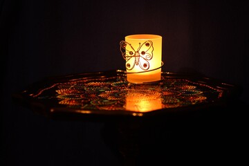 Zapalona świeczka w ciemnym pomieszczeniu, na ręcznie malowanym małym stoliku.