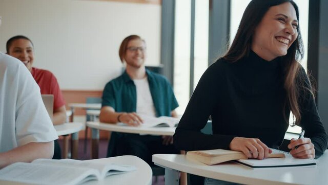 Girl attending the lecture and talking to the teacher. Smiling woman sitting in the classroom.

