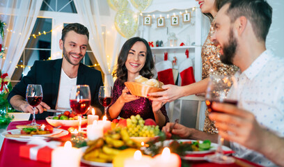 Group of happy excited beautiful friends while they are eating with glasses wine in hands at a home christmas party and having fun.