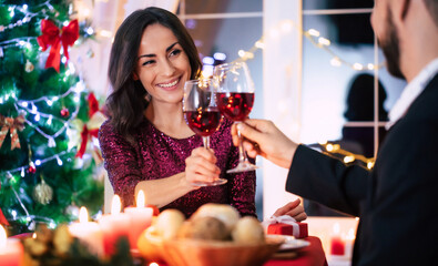 Happy beautiful elegant couple in love are sitting at christmas table and drinks wine from glasses.