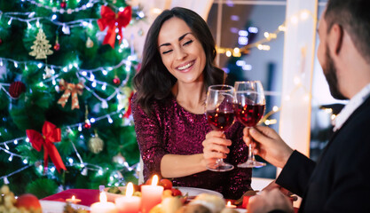 Happy beautiful elegant couple in love are sitting at christmas table and drinks wine from glasses.
