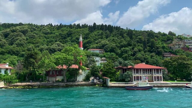 Footage of moored boats and luxury houses in upscale neighborhood called "Kandilli" by Bosphorus in Istanbul. It is a beautiful summer scene on cloudy summer day. Camera moves forward.