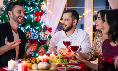 Group of happy excited beautiful friends while they are eating with glasses wine in hands at a home...