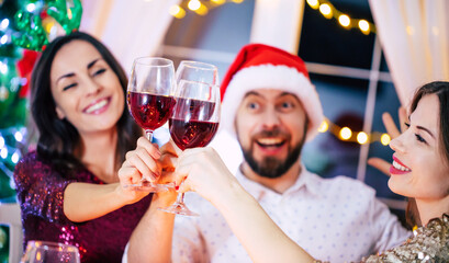 Group of happy excited beautiful friends while they are eating with glasses wine in hands at a home christmas party and having fun.