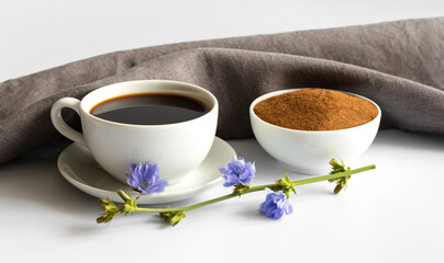 Cup with chicory drink, powder and blue flowers on white background. A useful coffee substitute.